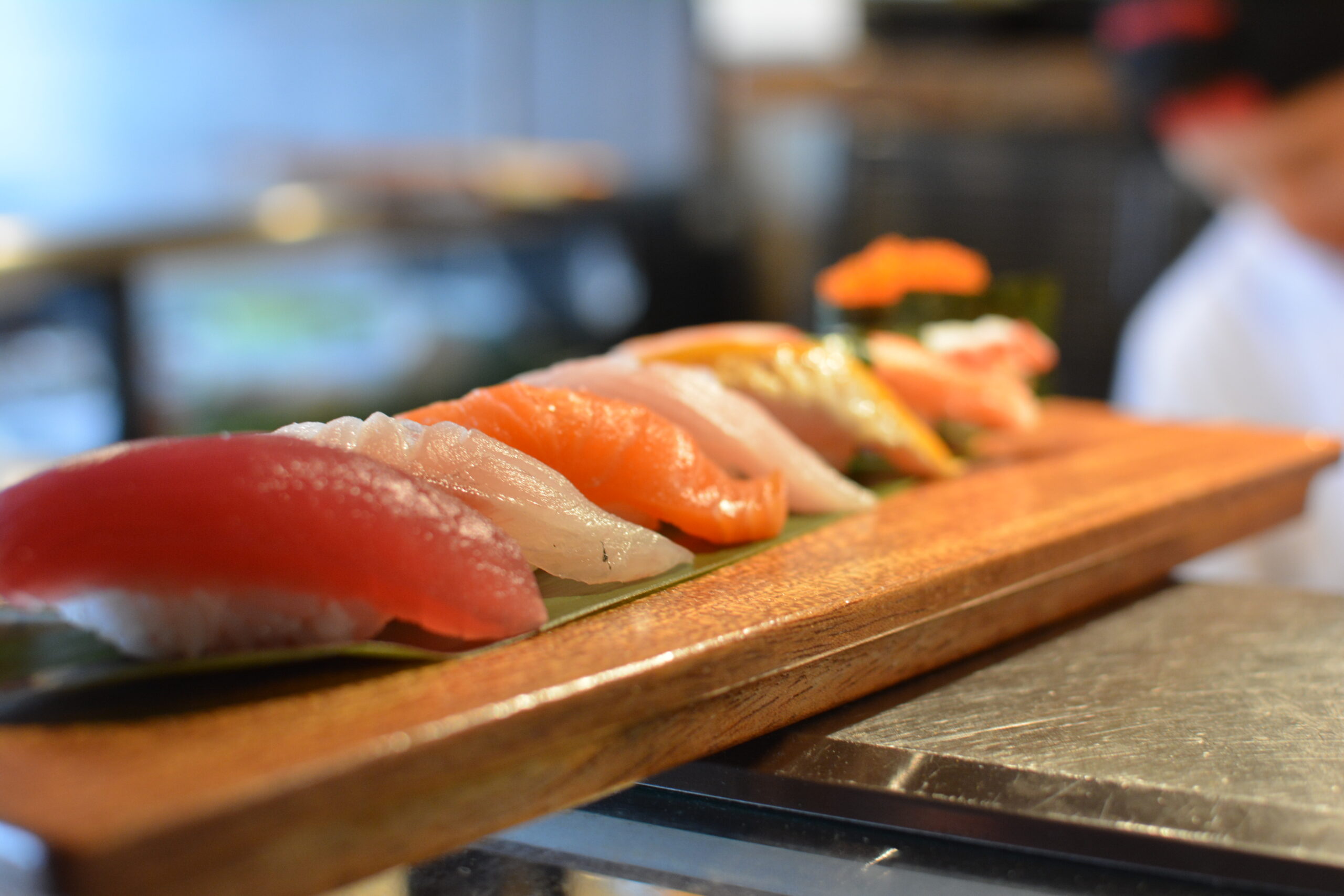 Fresh assorted nigiri sushi — tuna, salmon, and yellowtail — lined up on a wooden board at a Bay Area sushi restaurant, the kind of hero dish worth batch-photographing for a month of social media content.