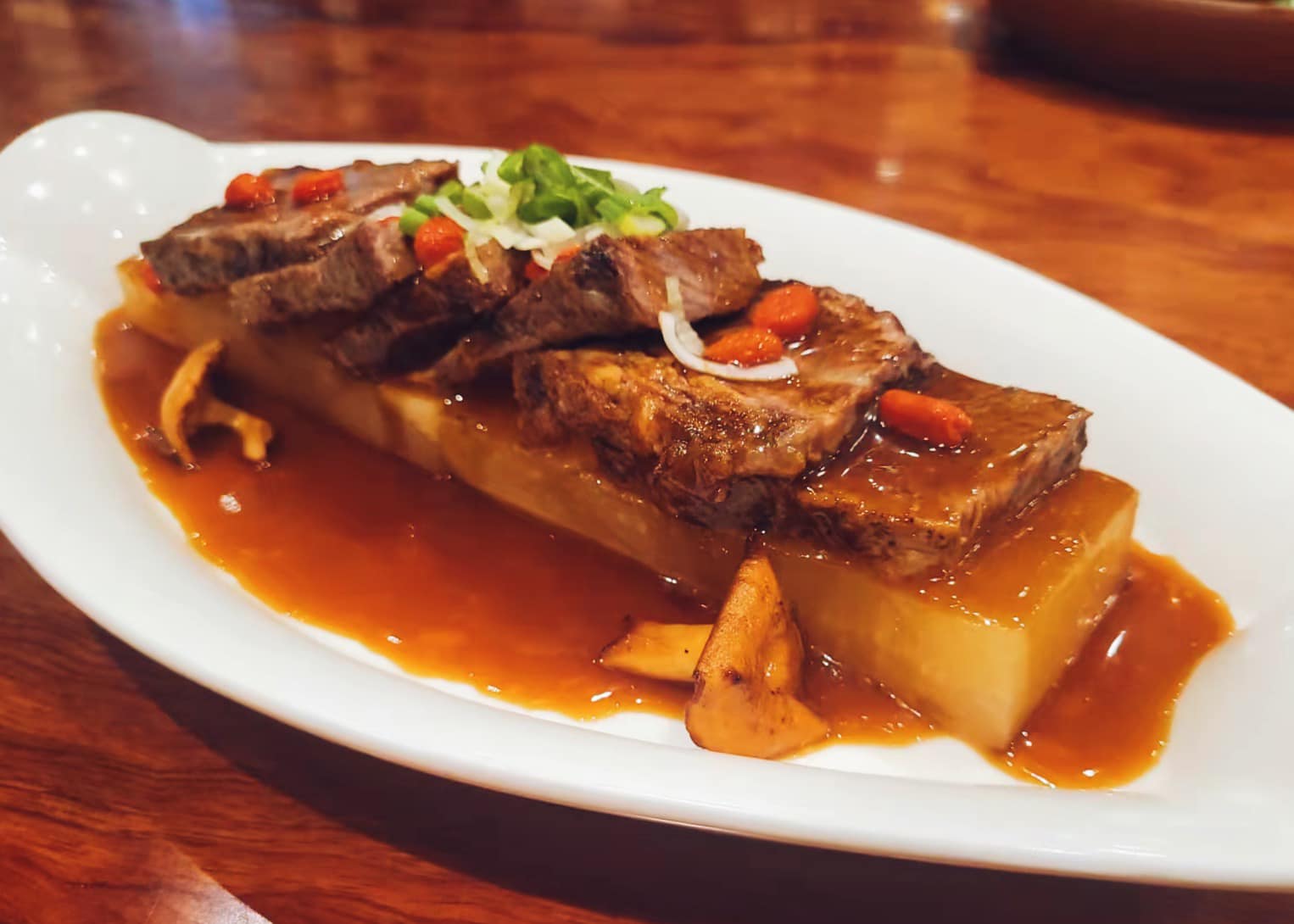 Braised short rib with daikon, hedgehog mushrooms and goji berries in a glossy brown sauce on a white platter at a Bay Area Chinese restaurant.