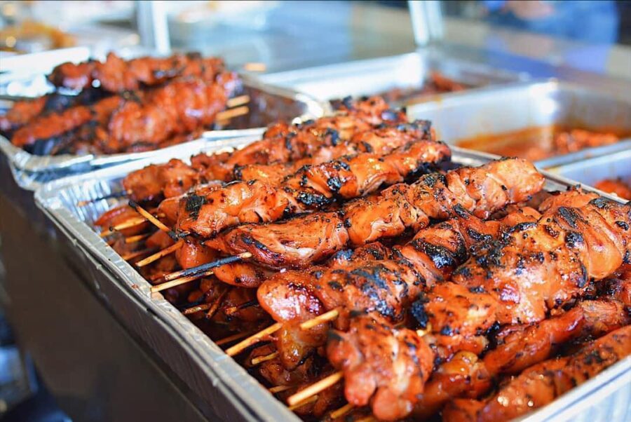 Foil catering trays filled with char-grilled chicken skewers, prepped for a large-format Bay Area restaurant catering order.