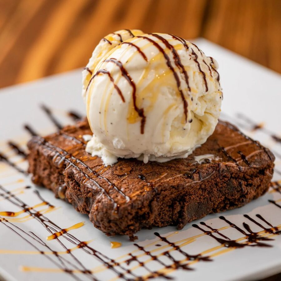 A warm chocolate brownie topped with a scoop of vanilla bean ice cream and drizzled with chocolate and caramel, the kind of on-the-house surprise that turns a Bay Area restaurant’s first-time guests into loyal regulars.